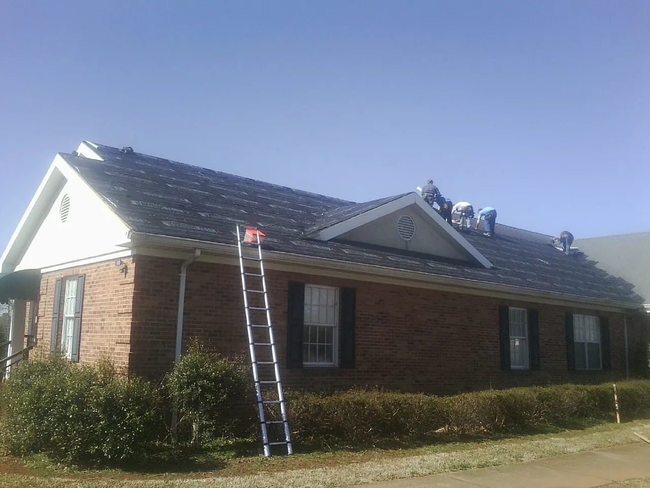 Crew tearing shingles off a brick ranch roof with a ladder set — Metal Roof Repair work by our crew in Orland