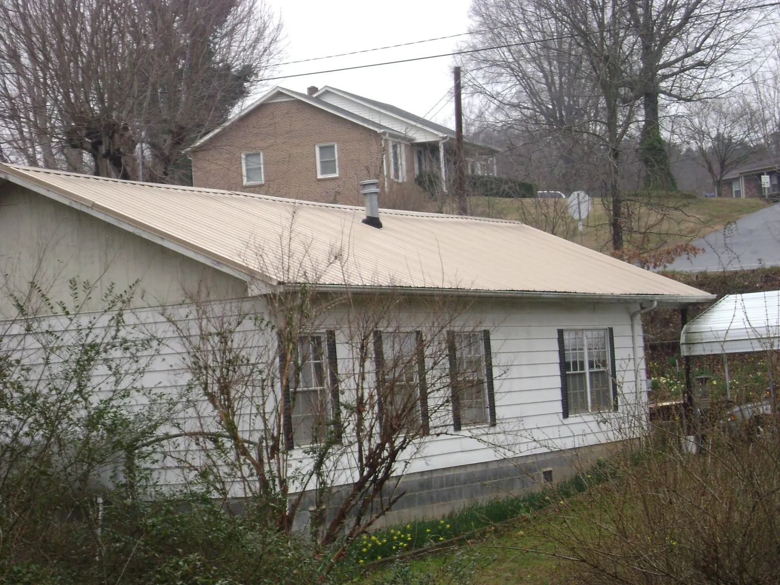 Tan metal roof on a white sided house set into a hillside — Commercial Roofing by Roofing Brothers in Orland